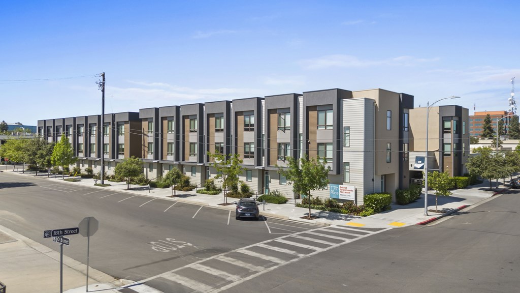 A street view of apartment buildings with a car parked on the side of the road.